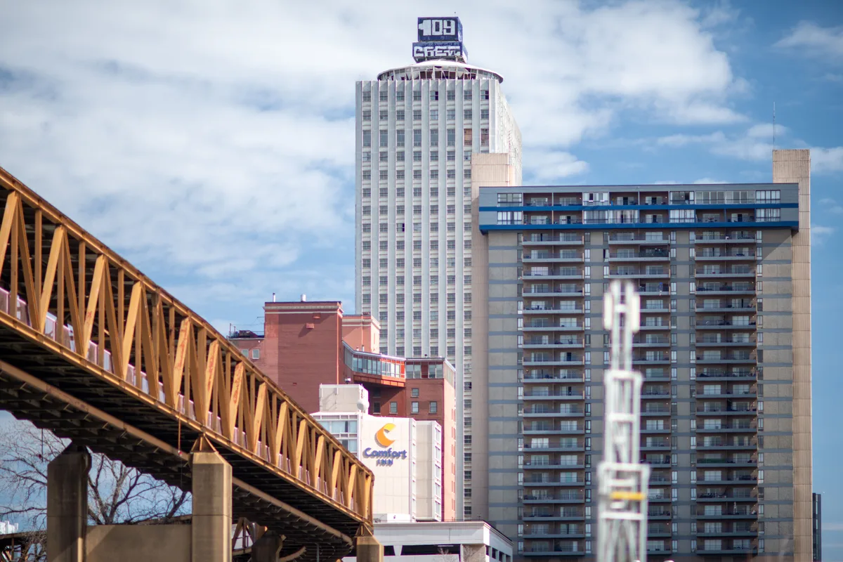 Downtown Memphis high-rises beside a rust-colored steel truss bridge under blue sky